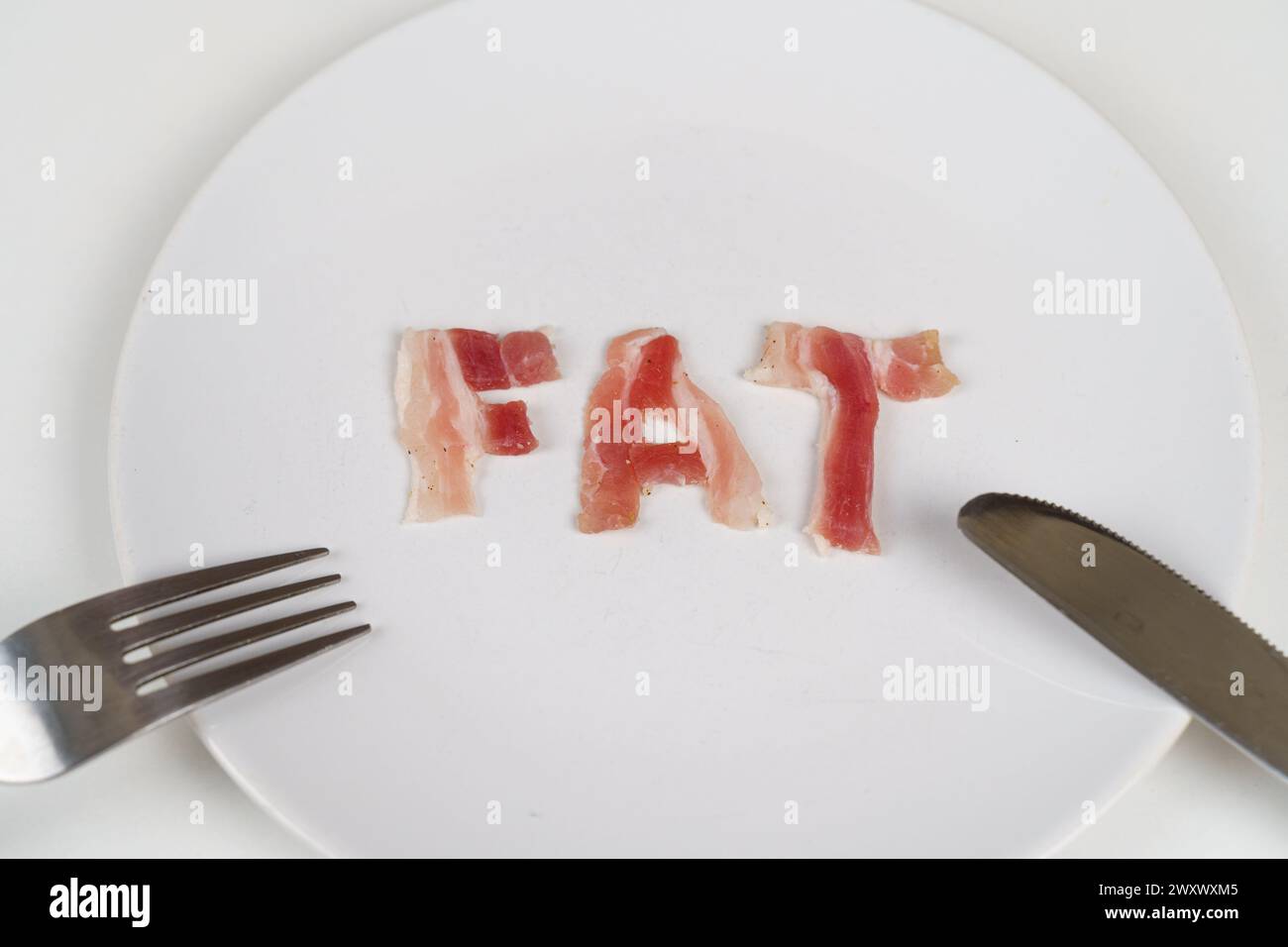 A plate with the word fat on it, accompanied by a fork and knife, symbolizing unhealthy eating habits. Stock Photo