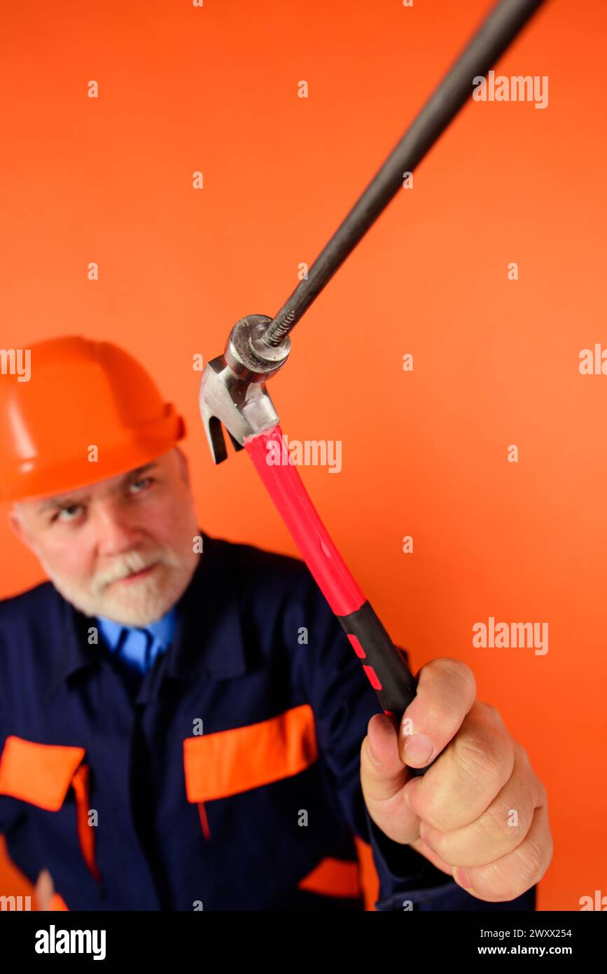 Construction worker or master in helmet hammering nails with hammer. Selective focus. Repairman or carpenter in hard hat hammers nail. Builder with Stock Photo