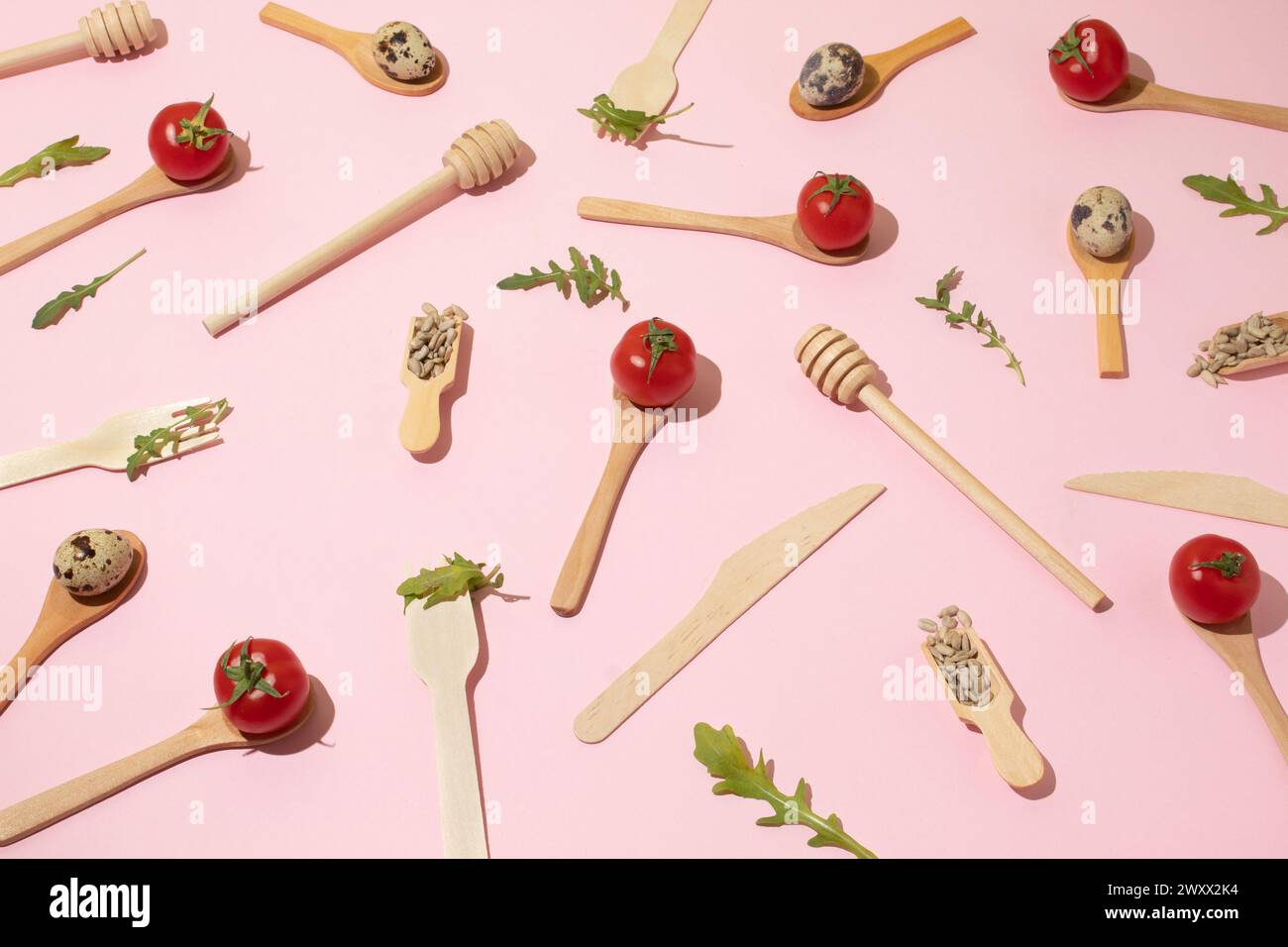 Wooden kitchen cutlery, cherry tomatoes, quail eggs, sunflower seeds on pink background. Flat lay pattern Stock Photo