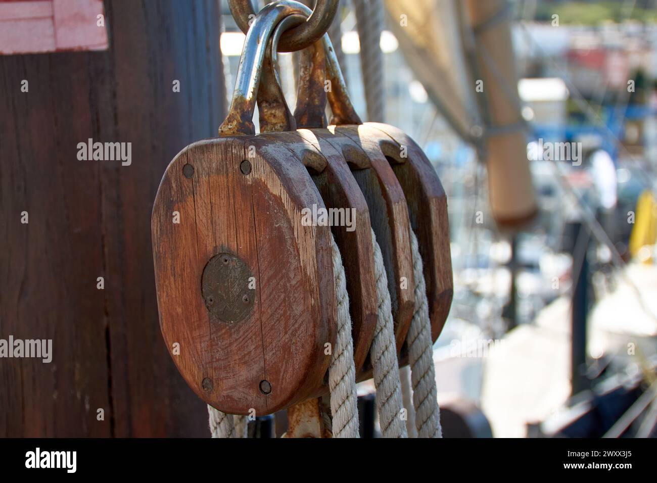Pulley for sails and ropes made of wood on the replica of the Santa Maria caravel, with the sail and other ships in the harbor, soft and out of focus Stock Photo