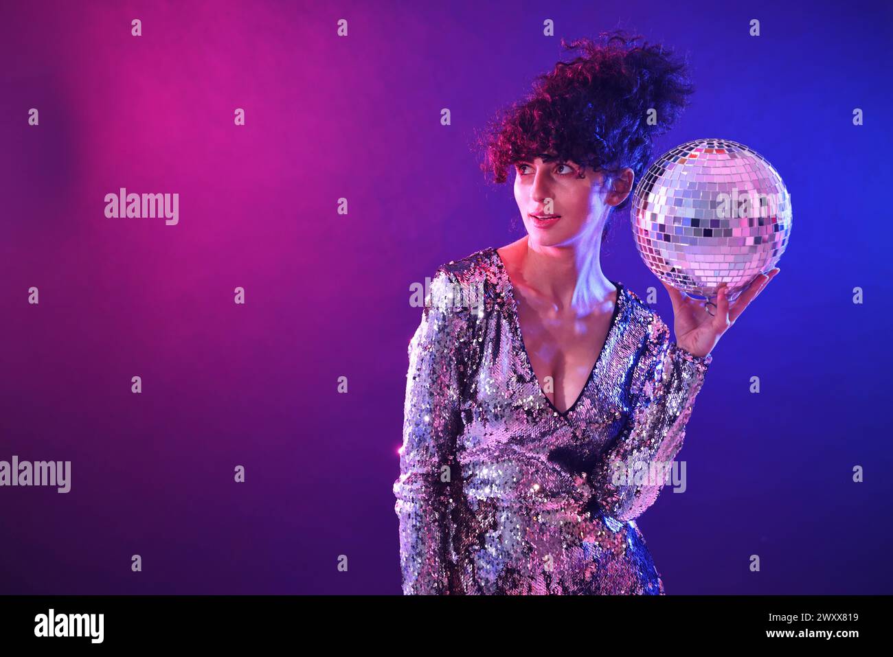 Beautiful young woman with disco ball posing on color background in neon lights. Space for text Stock Photo