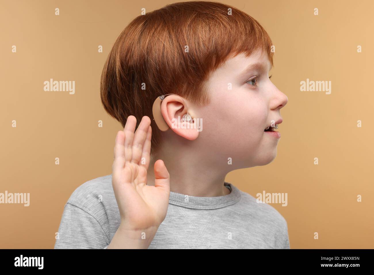 Little boy with hearing aid on pale brown background Stock Photo