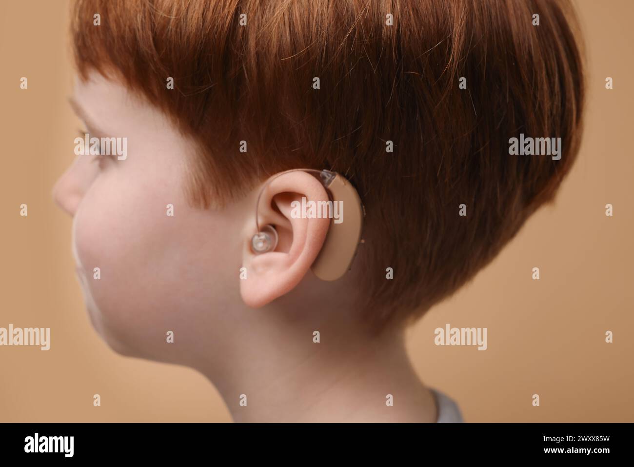 Little boy with hearing aid on pale brown background, closeup Stock Photo