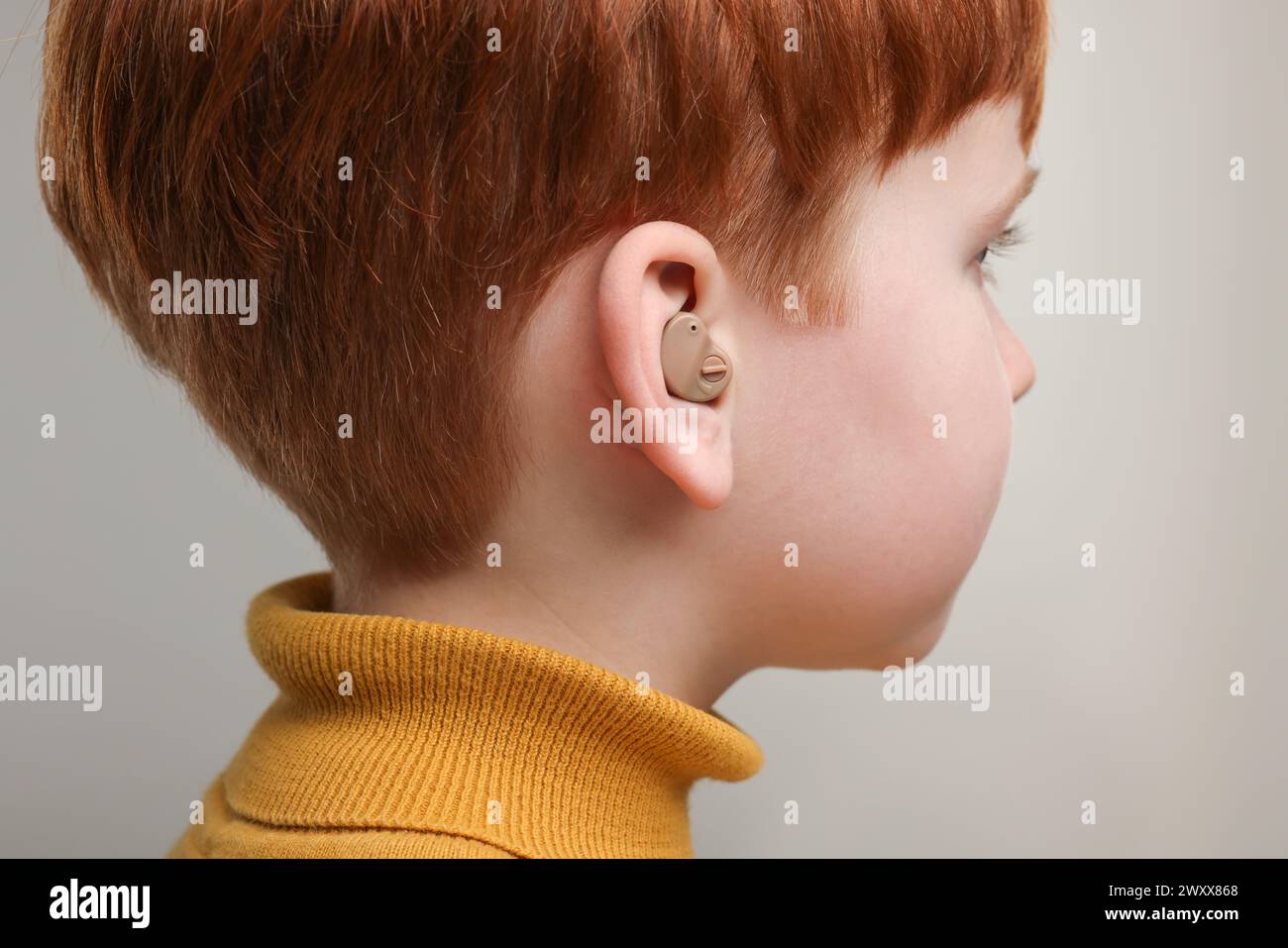 Little boy with hearing aid on grey background, closeup Stock Photo