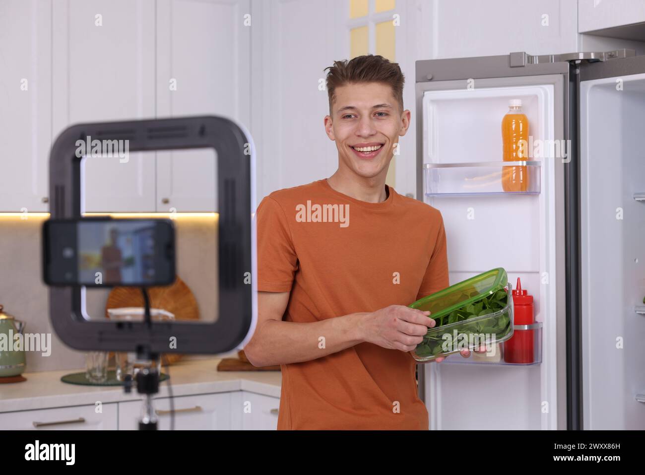 Smiling food blogger explaining something while recording video in kitchen Stock Photo