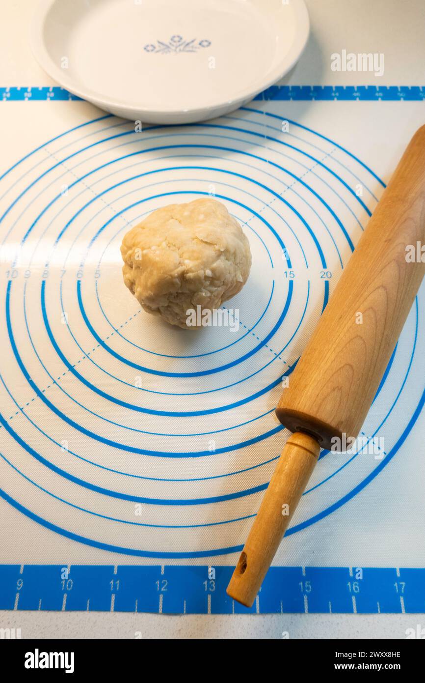Plastic measuring sheet for a ball of pie dough sitting in the middle with a pie plate and rolling pin. Stock Photo