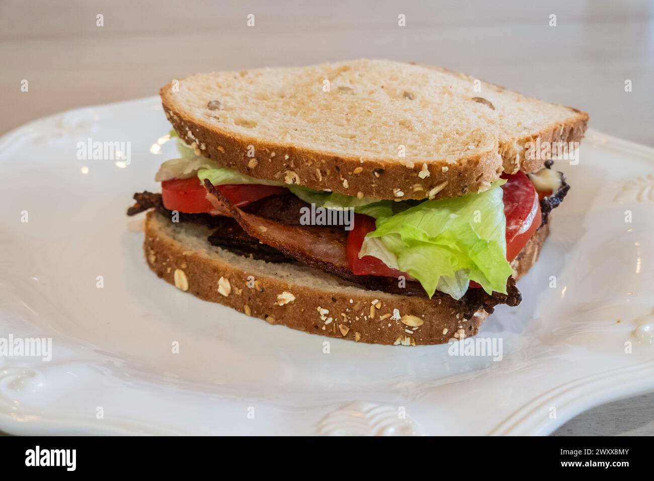 BLT, Bacon, lettuce & tomato sandwich  with oatnut bread & mayo on a white plate. Stock Photo