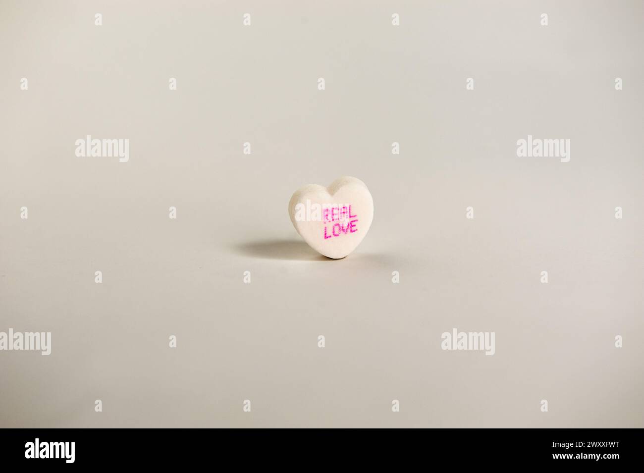 single candy heart on a white background that says 'real love' Stock Photo