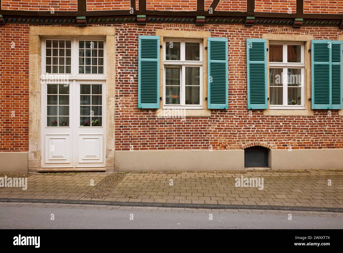 White entrance door and windows with blue-green shutters on a brick house in Warendorf, Warendorf district, North Rhine-Westphalia, Germany Stock Photo