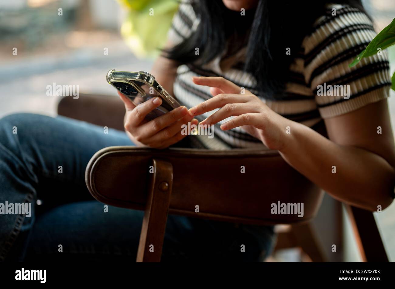 A cropped image of an Asian woman using her smartphone while relaxing ...