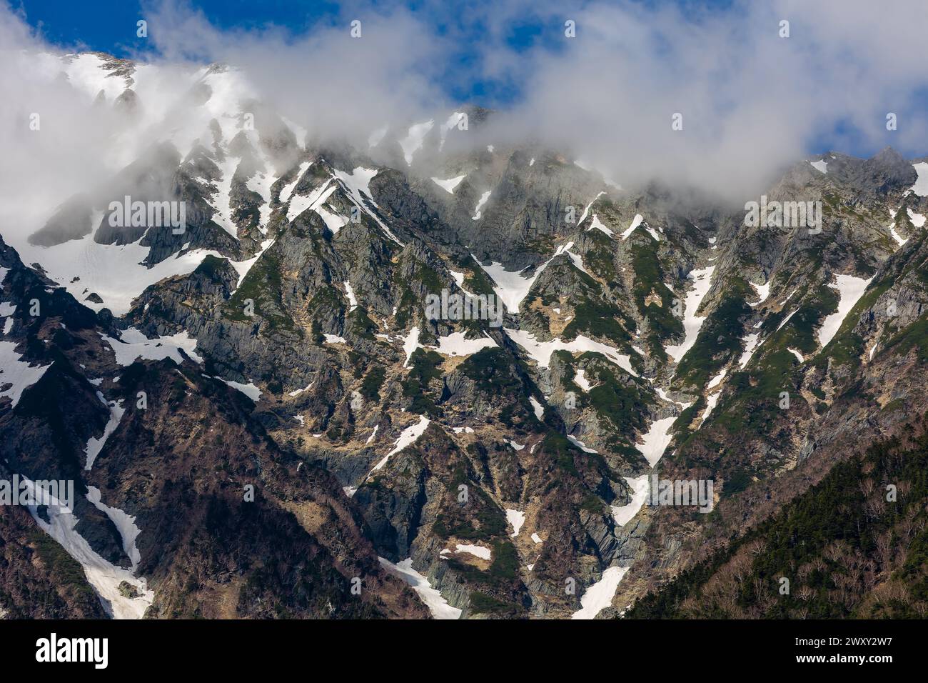 Clouds over the top of tall, jagged, snow covered mountain peaks Stock ...