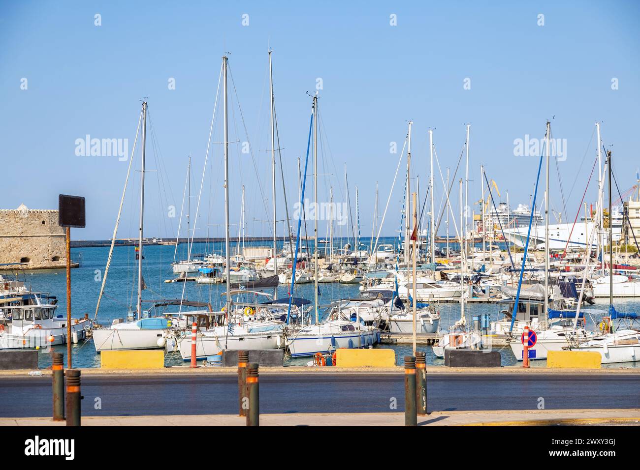 Crete island, destination Greece. Moored ship and boat with mast at Heraklion old Venetian harbor, calm sea water, blue sky background. Stock Photo