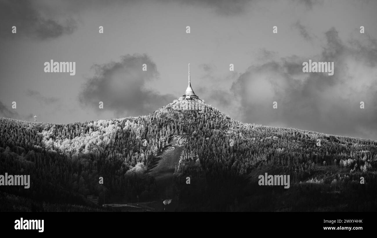 A crisp morning view of the snow-covered Jested peak with its iconic tower standing tall against a blue sky. Liberec, Czechia. Black and white image. Stock Photo
