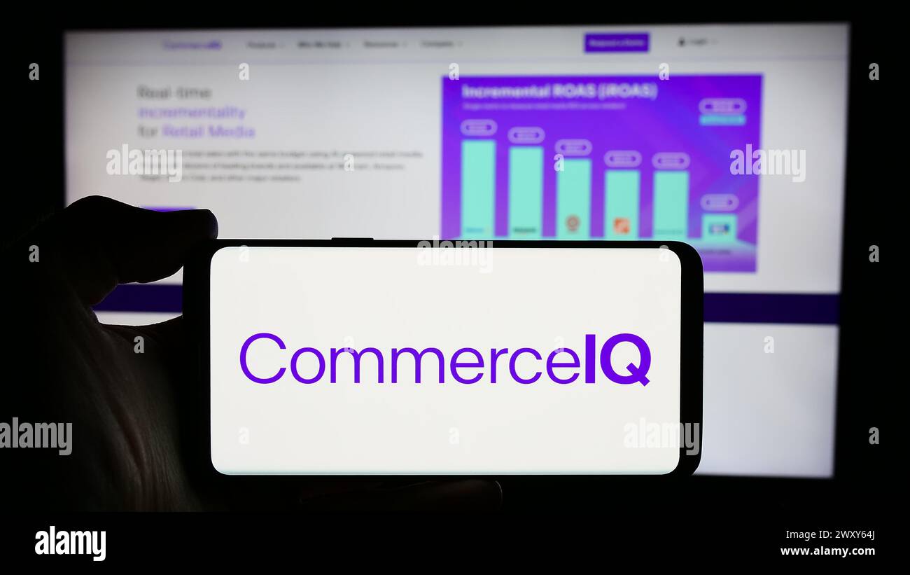 Person holding smartphone with logo of US e-commerce management company CommerceIQ Inc. in front of website. Focus on phone display. Stock Photo