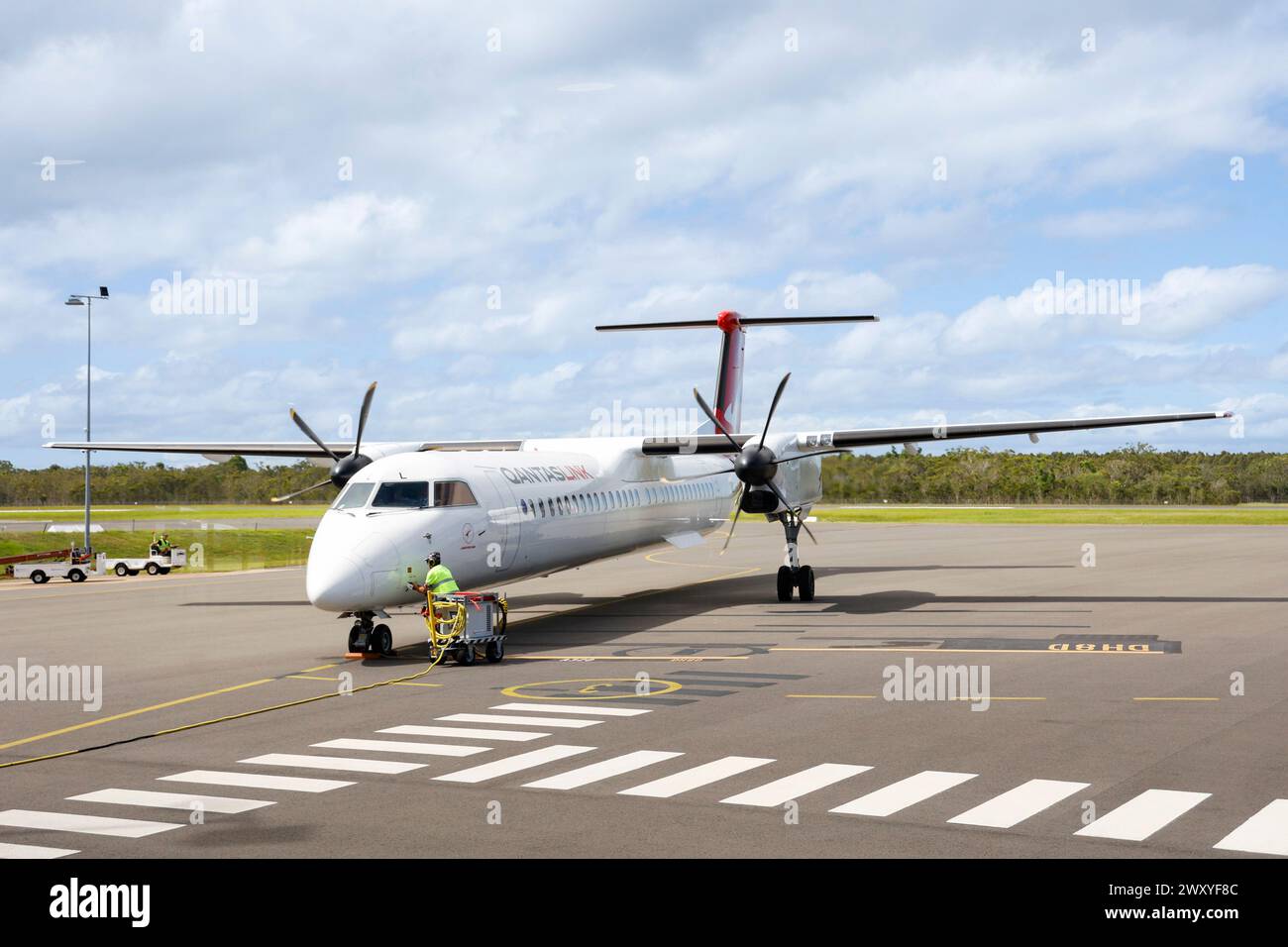 Service man charging Qantaslink Dash 8 regional turboprop plane on runway at Hervey Bay airport, Queensland, Australia Stock Photo