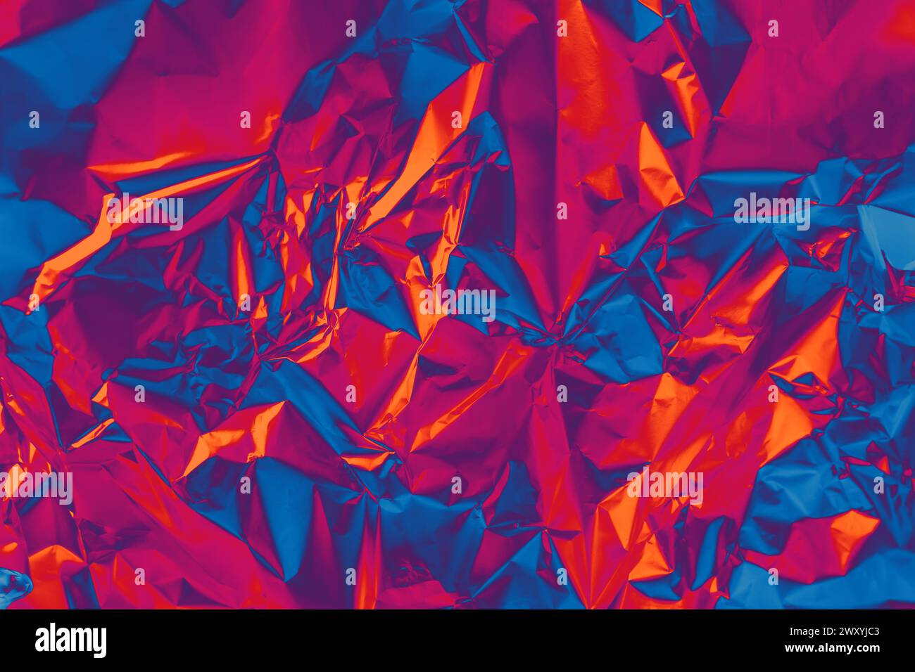 Photo texture of glossy metal surface in holographic spectral palette. Shiny foil in orange, purple, very peri, blue color background Stock Photo