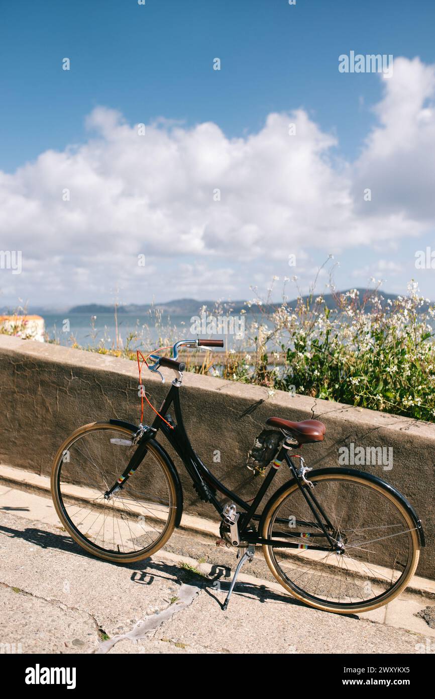 A classic black bicycle with a leather saddle rests against a sea wall, overlooking the scenic San Francisco Bay in springtime Stock Photo