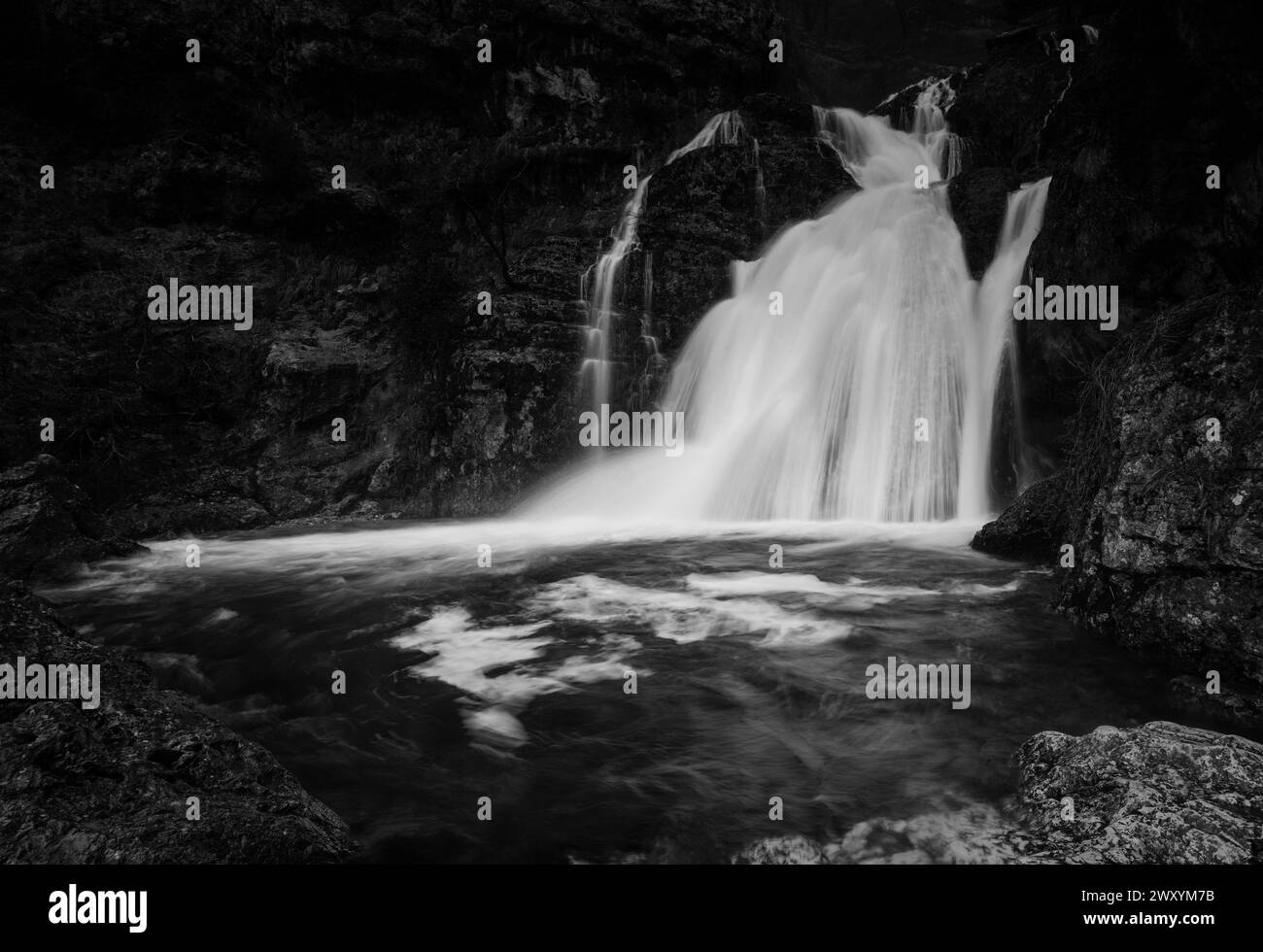 A black and white portrayal of the Rio Mundo Waterfall's vigorous cascade, creating a striking contrast with the surrounding rocks Stock Photo