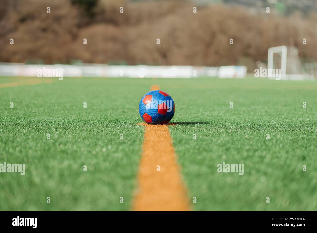 Close-up of a colorful soccer ball placed on the green grass of a soccer field, perfectly aligned with the midfield line, with goalposts visible in th Stock Photo