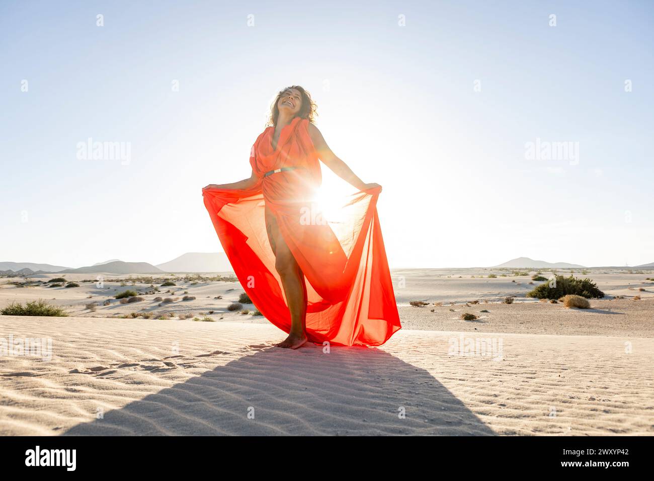 Elegant woman in a flowing red dress poses on desert dunes with her eyes  closed, basking in the golden sunlight Stock Photo - Alamy