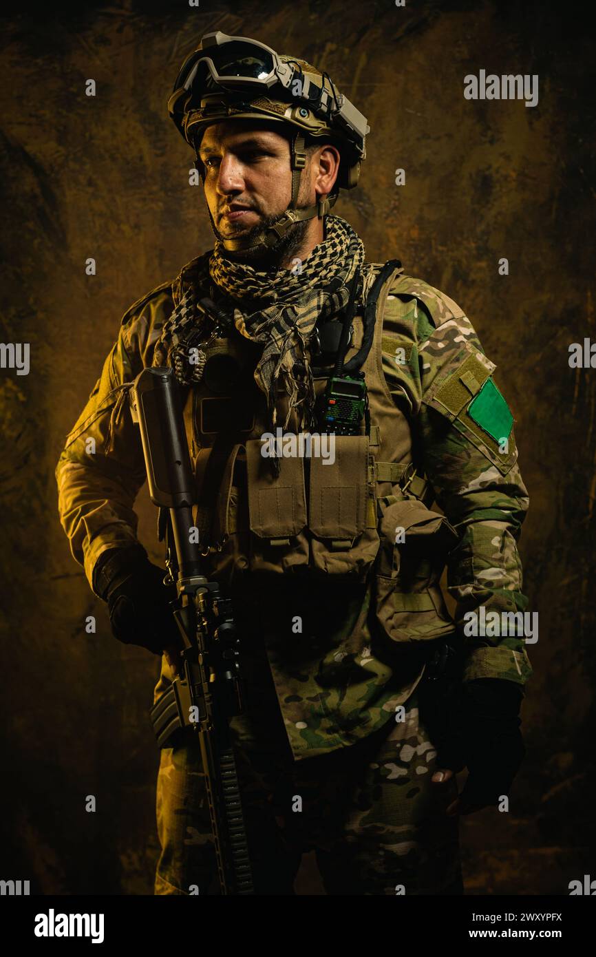 A focused Latin American soldier clad in tactical gear stands ready, exuding confidence and preparedness in a rugged backdrop Stock Photo