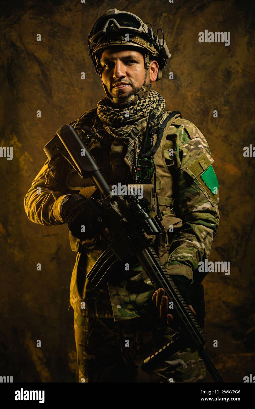 A portrait of a resolute Latin American soldier in full gear, posing with his rifle against a textured backdrop Stock Photo