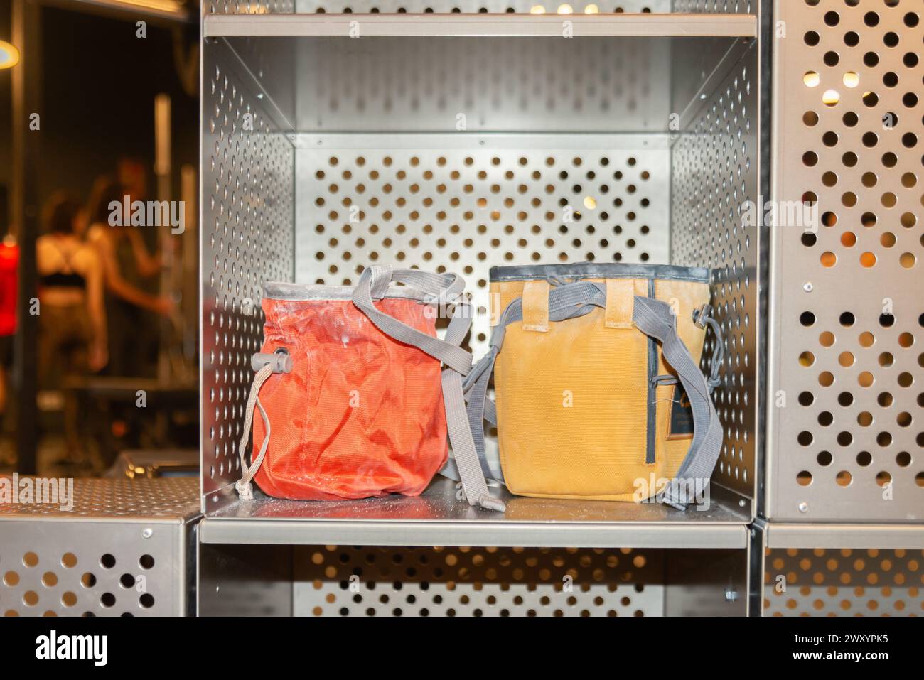 Red and mustard backpacks neatly placed on a shelf of a metal locker, indicating an organized storage space in a public area Stock Photo