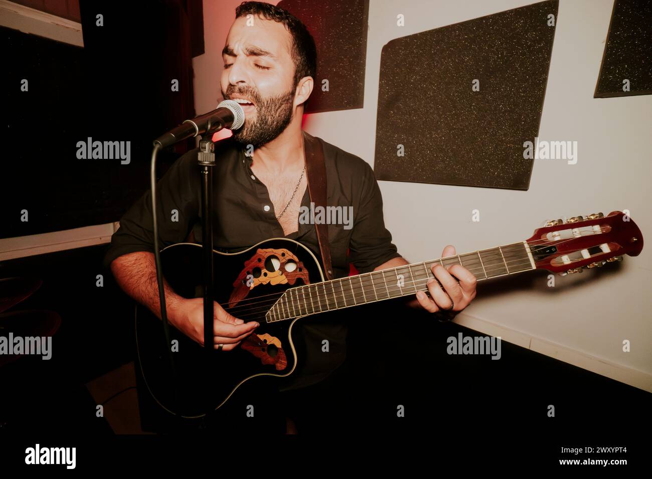 Male musician passionately singing and playing an acoustic guitar at a live performance. Stock Photo