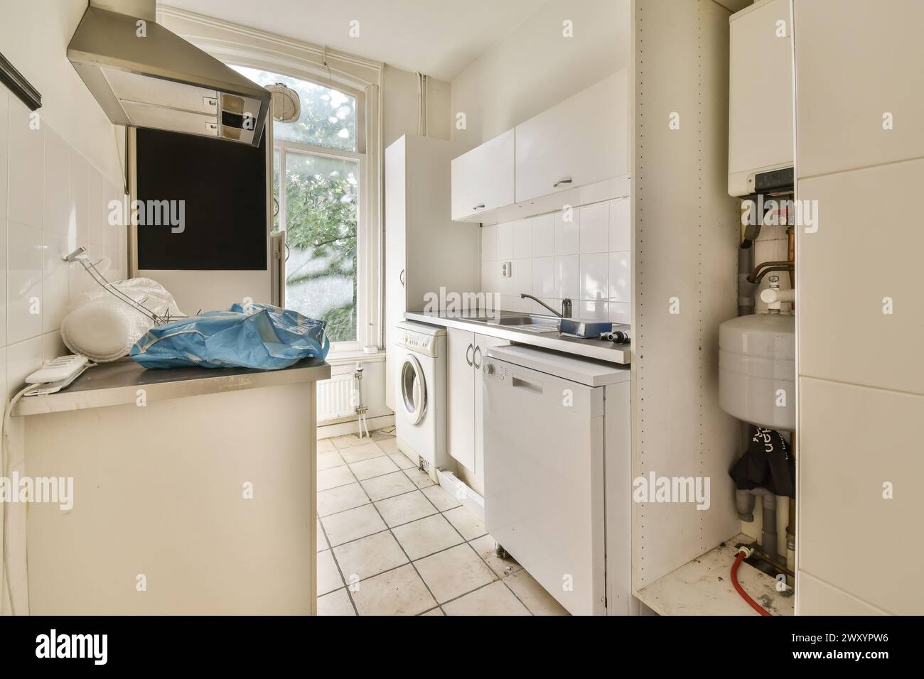 An image of a small, cluttered urban kitchen featuring basic appliances, a window, and tiled flooring. Stock Photo