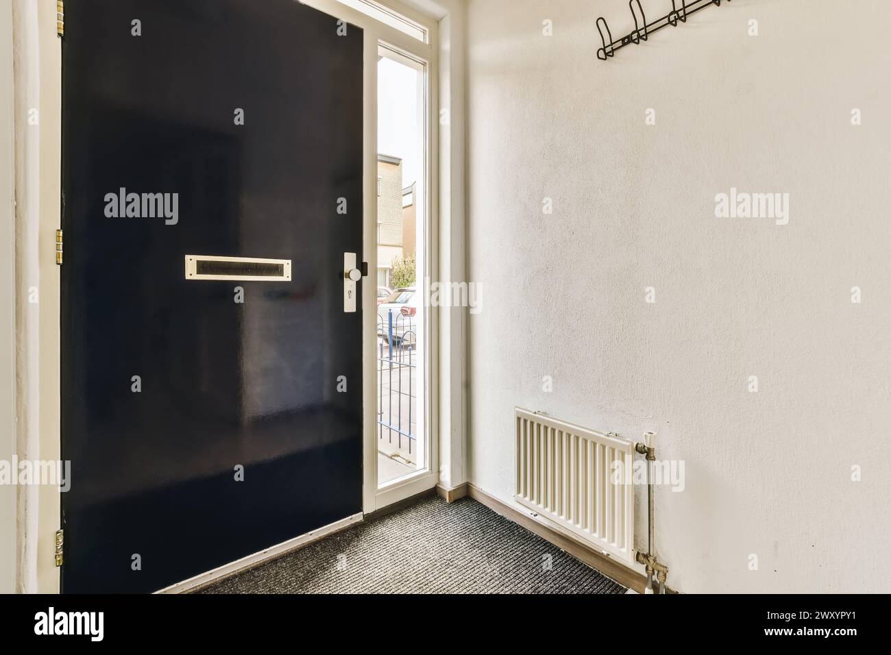 An inviting residential entryway with the front door open, showcasing a view of the street and coat hooks on the wall. Stock Photo