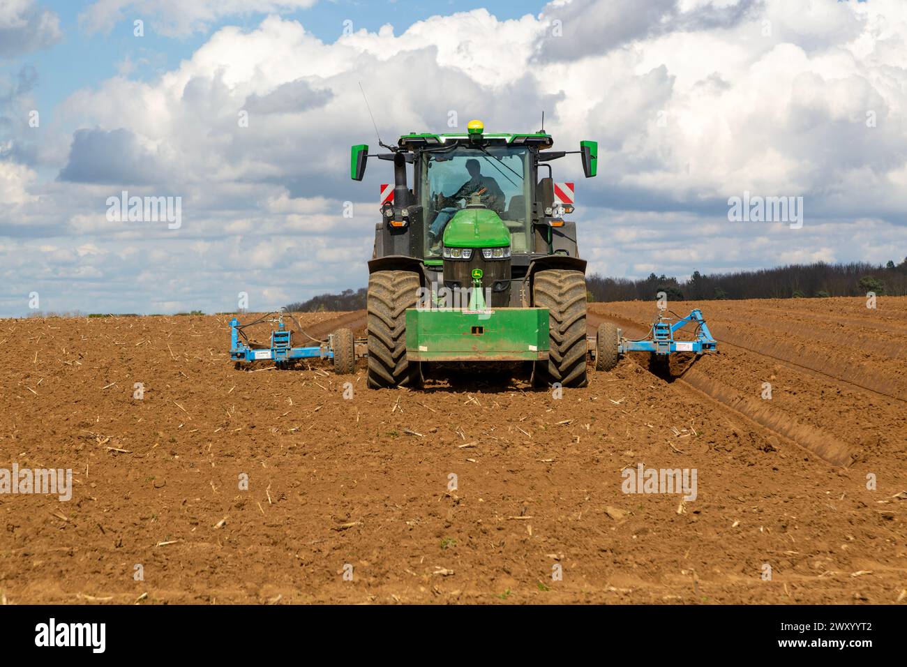 Green John Deere tractor ploughing deep furrows to prepare soil for potato crop, Ramsholt, Suffolk, England, UK Stock Photo