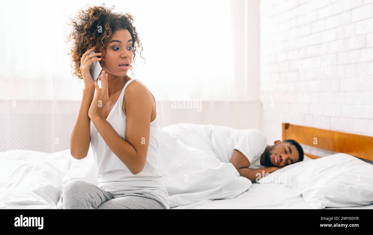 Woman on phone with man asleep in bed Stock Photo