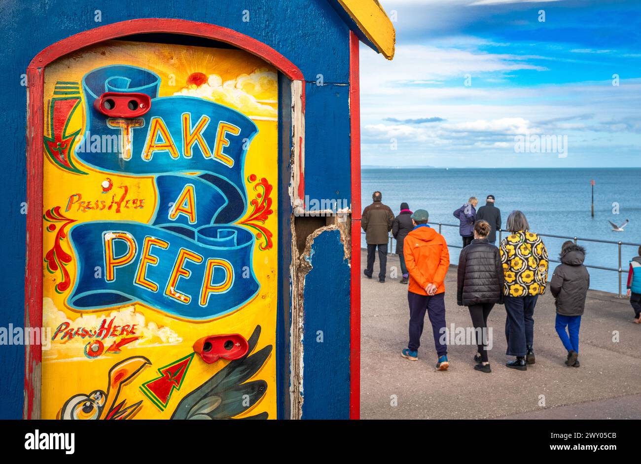 People walk past an old fashioned peep show booth on the seafront