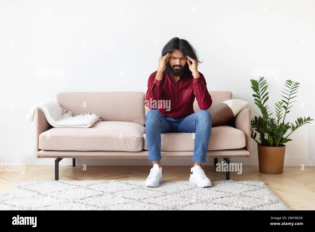Man with headache sitting on couch at home Stock Photo