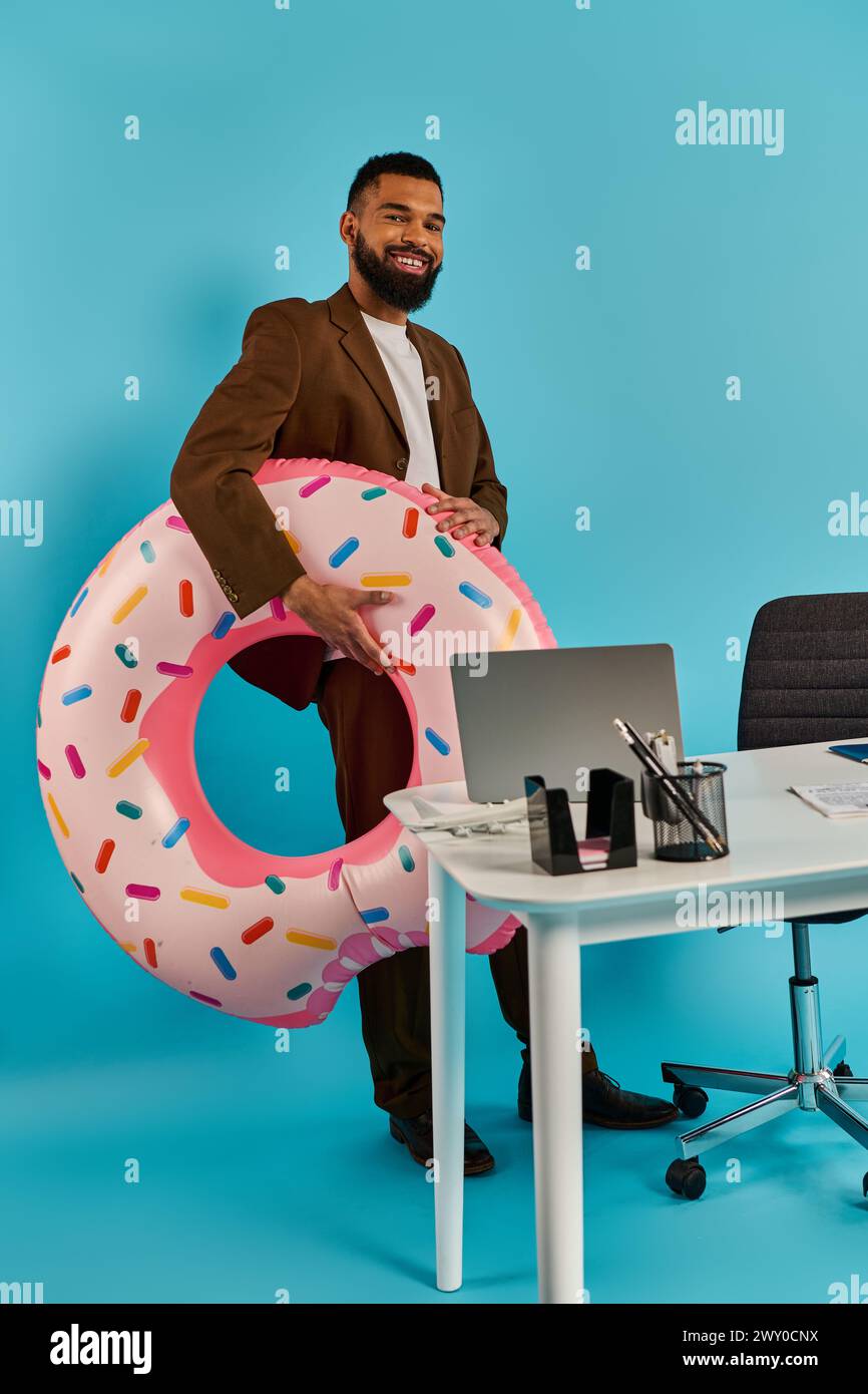 A man sits at a desk, staring at a massive donut in front of him. The donut is larger than life, enticing and surreal. Stock Photo