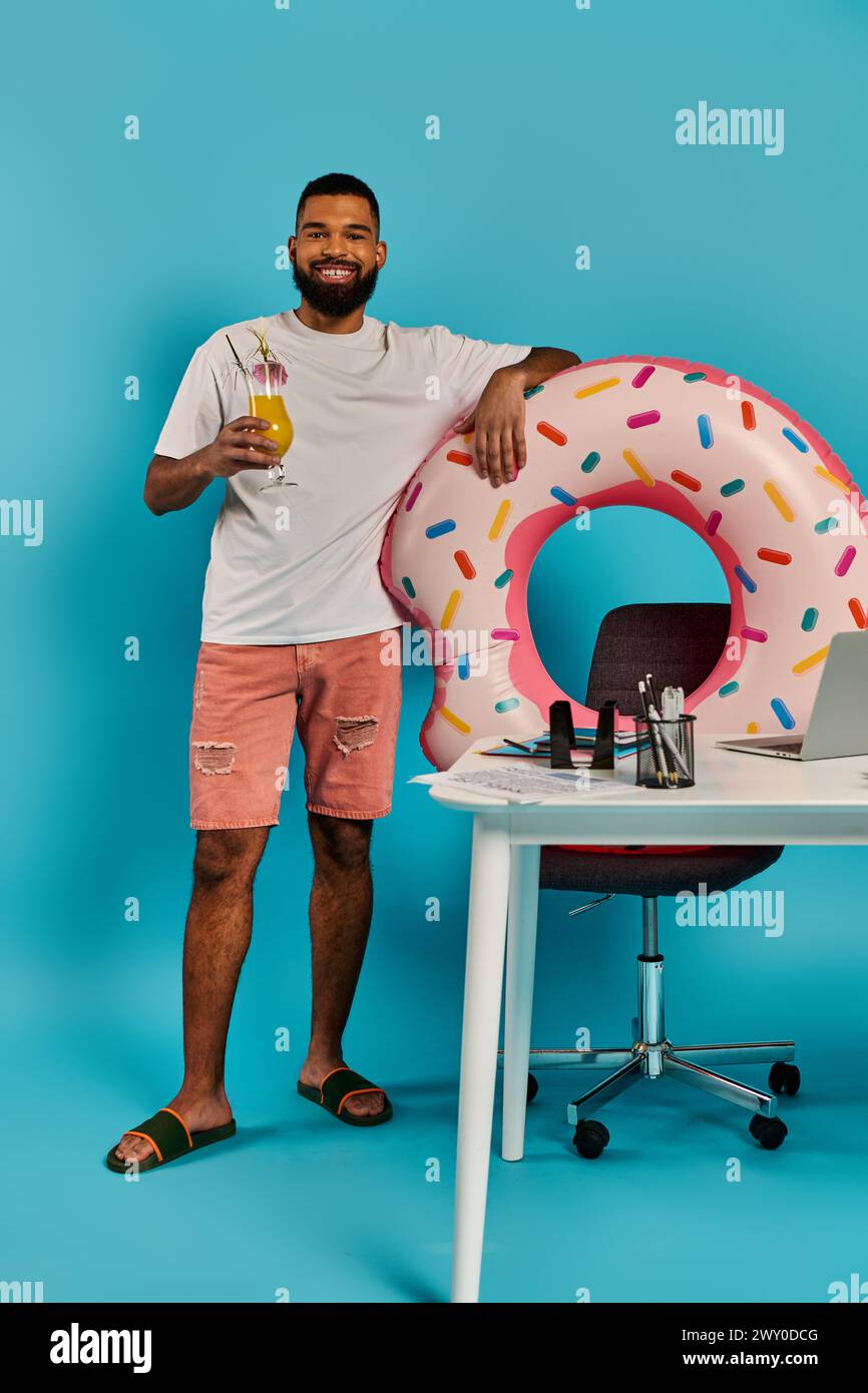 A man standing next to a desk, looking excited, with a giant donut placed on it. Stock Photo