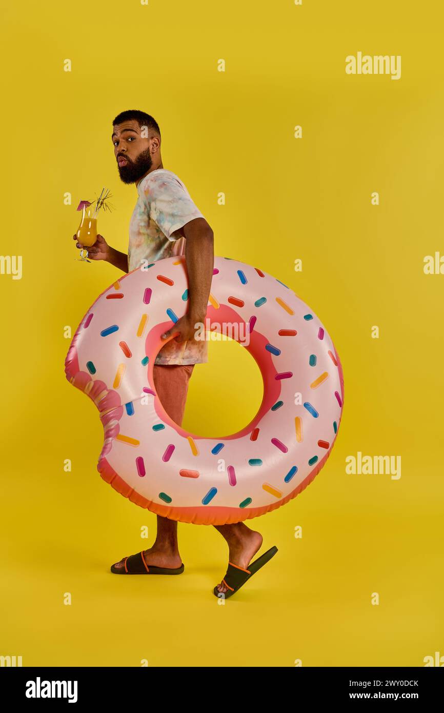 A man joyfully holds a gigantic donut in one hand and a glass of beer in the other, showcasing a unique and delicious pairing of treats. Stock Photo