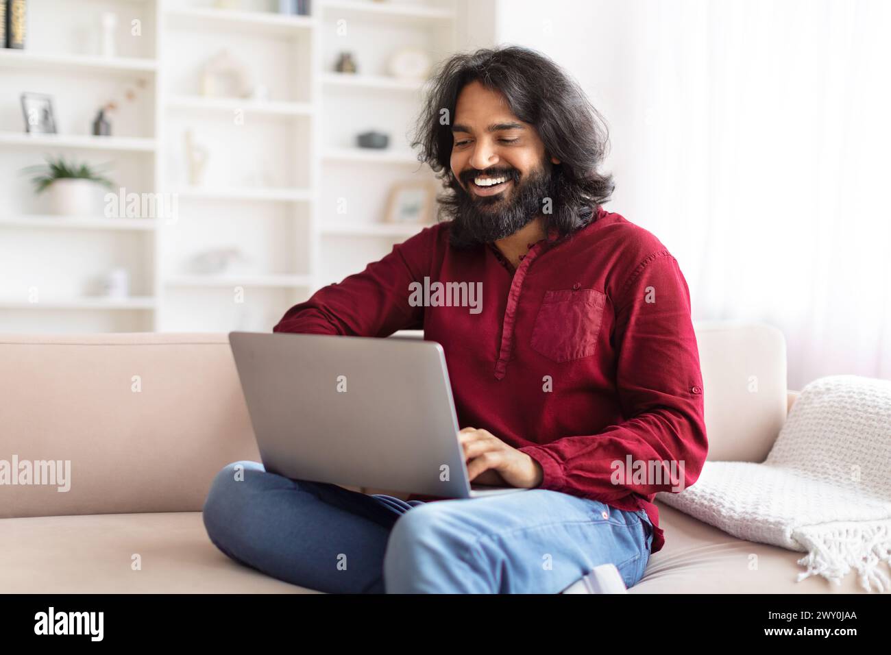 Man laughing while using a laptop on sofa Stock Photo