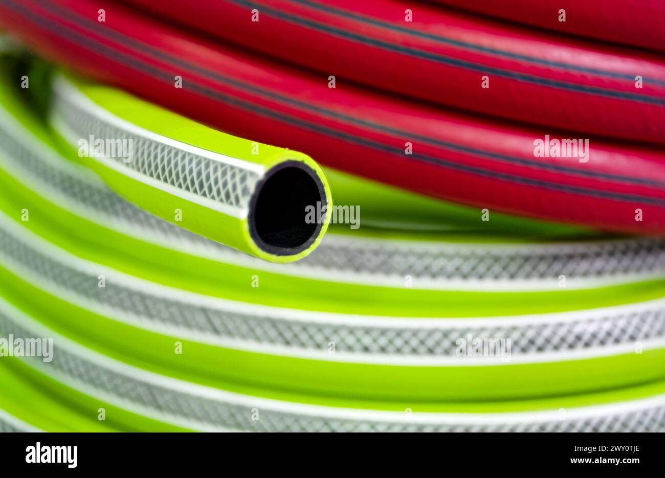 Rolled up colourful garden hose, red and green, close-up shot, selective focus, abstract gardening background Stock Photo