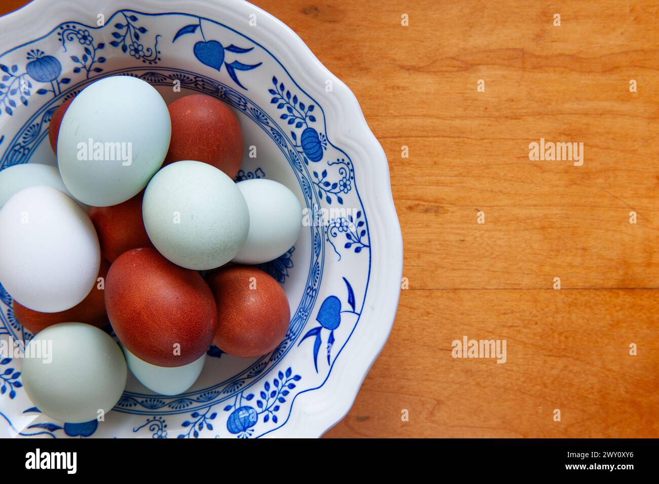 Farm fresh eggs in a white and blue china bowl on a wooden table Stock Photo