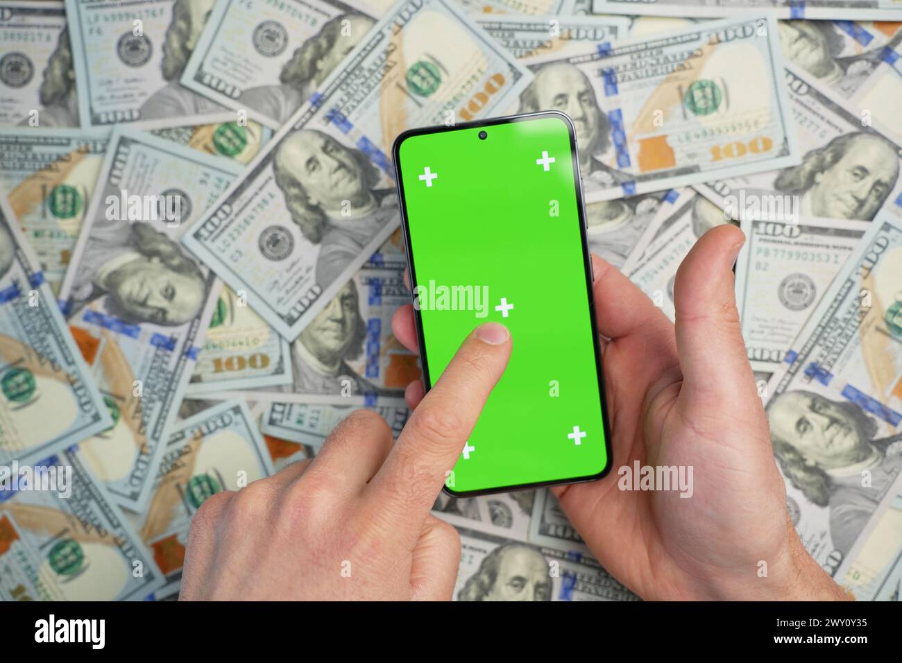 Hand holding smartphone with green screen on pile of dollar banknotes, top view. Concept of online earnings Stock Photo