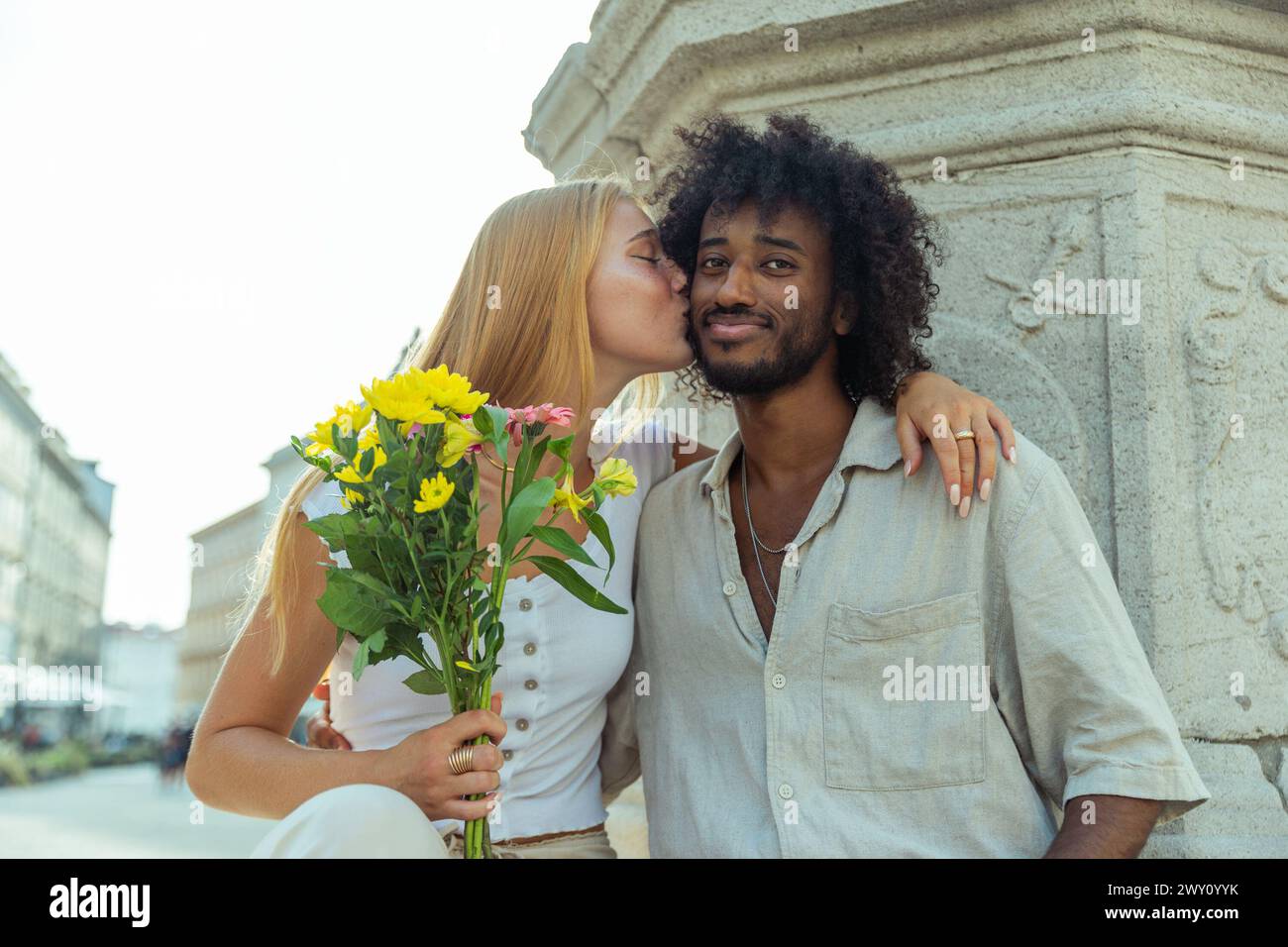 Boyfriend receives a kiss from his girlfriend after giving her a bouquet of flowers, mixed couple. Stock Photo