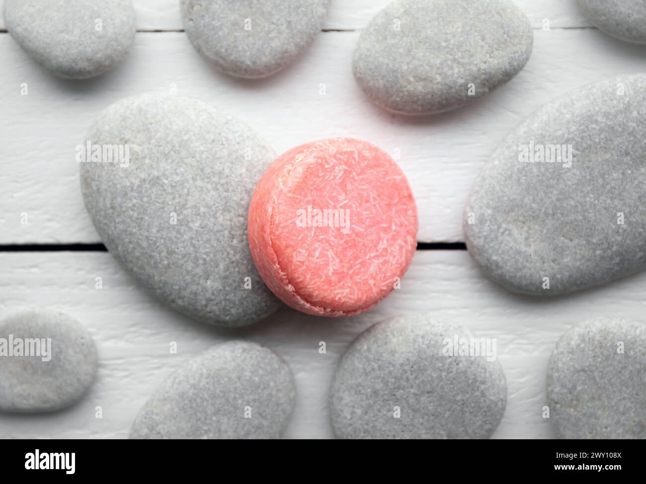 Flat lay view of pink color solid shampoo bar, conditioner bar on flat sea stones. Minimalist beauty set indoors. Shallow depth of field. Stock Photo
