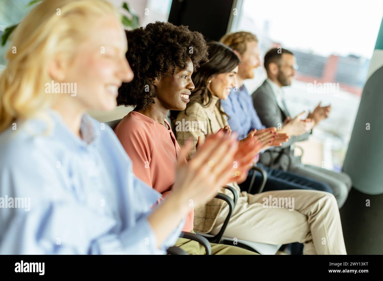 Smiling woman leads a round of applause with peers, sharing a moment of joy Stock Photo