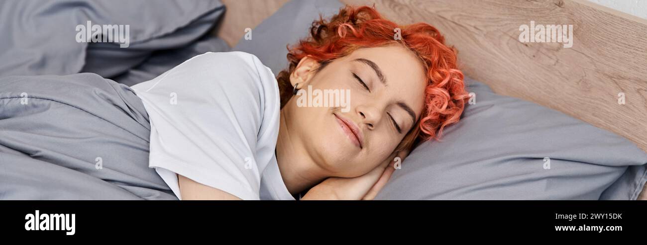 good looking red haired queer person in homewear napping in her bed at home, leisure time, banner Stock Photo