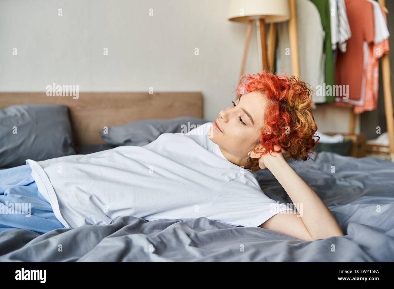 beautiful extravagant person with red vibrant hair lying in her bed and looking away, leisure time Stock Photo