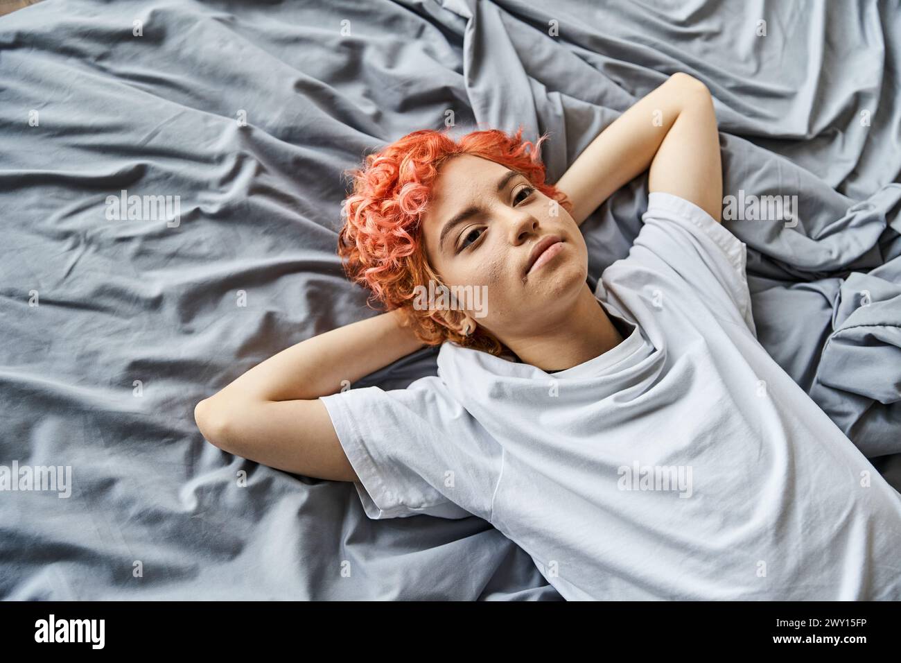 appealing extravagant person with red vibrant hair lying in her bed and looking away, leisure time Stock Photo