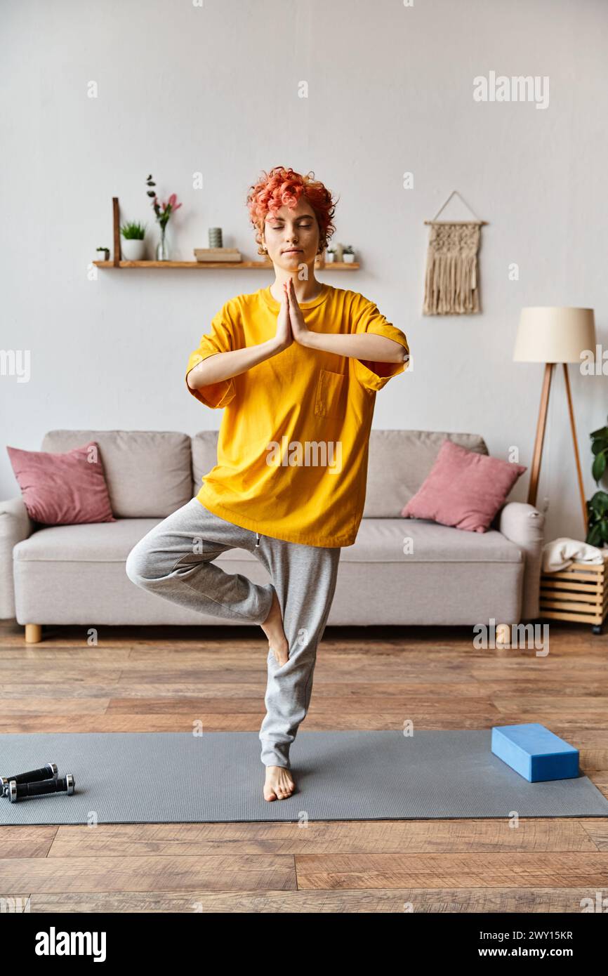 attractive red haired queer person in vivid outfit meditating with closed eyes while at home Stock Photo