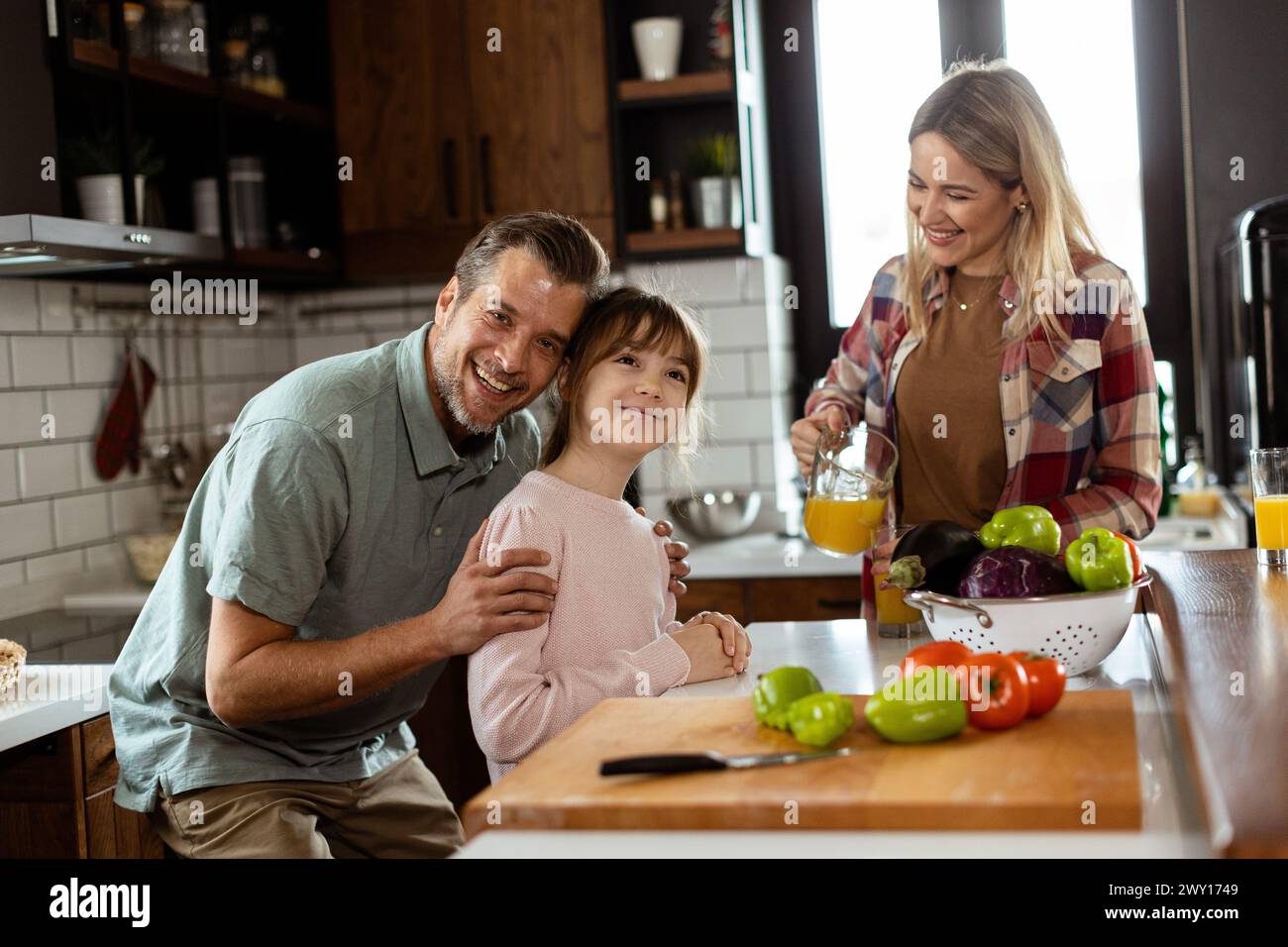 Young family chatting and preparing food around a bustling kitchen counter filled with fresh ingredients and cooking utensils Stock Photo