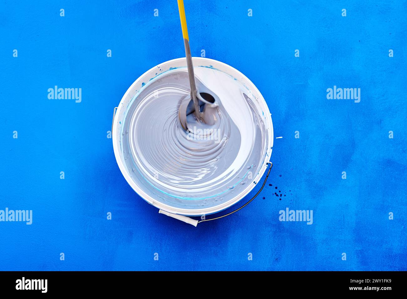 Top view captures process of stirring rod mixing fresh, white paint in ...